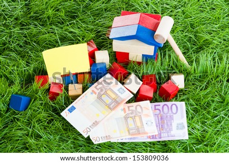Small house of children\'s blocks, the money lying in the grass.