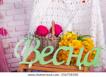 spring still life with the word Spring and yellow flowers on a background of knitted plaid with a ball of knitting