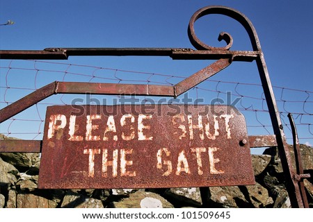 A metal rusty sign on an old gate  with the words 'PLEASE SHUT THE GATE'.
