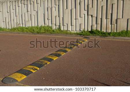 A black and yellow speed bump, rumble strip stretches across a red tarmac road.