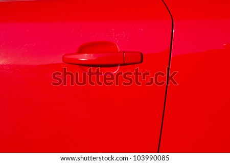 A glossy red painted car door with door edge and a handle.