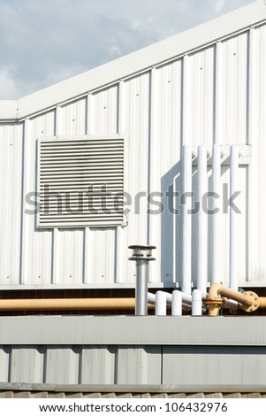 A section of an industrial unit with vent panel and a variety of piping.