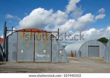 An industrial unit made from corrugated metal sheets with a sliding shutter and door on rough ground.