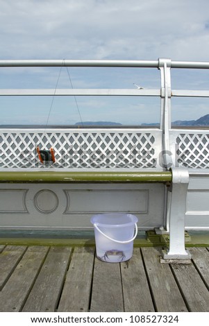 A crab line reel attached to a seat railing with a clear plastic bucket with a crab in water.