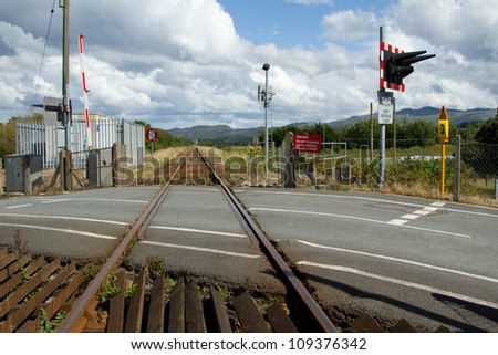 A rail line stretches into the distance with a tarmac road level crossing with safety markings, signs, lights and barriers.