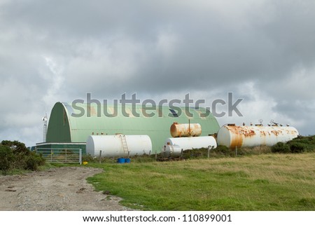 A track leads to a gate with white coloured chemical tanks and a green metal work shed.