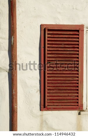 A rustic wooden, brown painted, window shutter and downpipe on a cream painted stone wall.