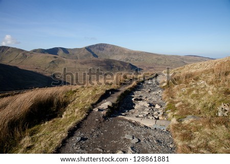 A mountain footpath with a drainage pipe crossing with mountains in the distance.