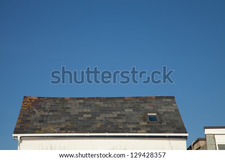A slate tile roof with sky light, ridge tiles and gutter against a clear blue sky.