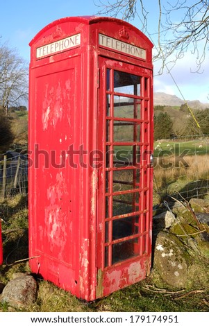 A vintage red British telephone box with flaking paint and \'telephone\' sign in a rural setting.