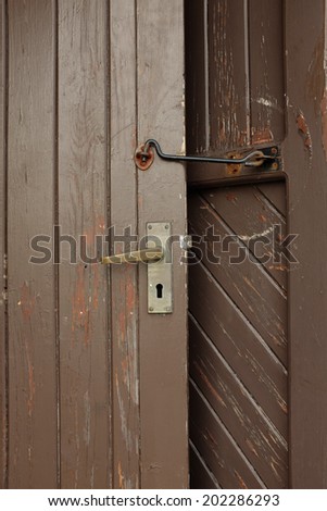 A brown painted door with a brass handle and lock held open by a metal hook.
