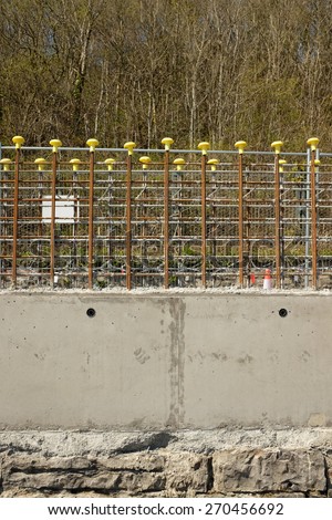A stone wall with new concrete cast in a section with steel rods and yellow safety caps.