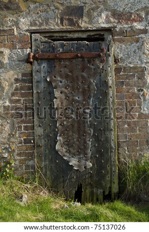 Old oak door with rusty hinge and a partial metal covering and reinforcing rivets.