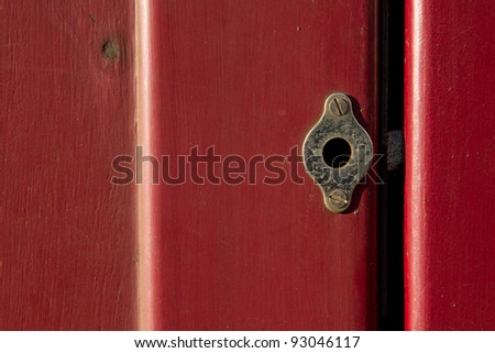 A vintage brass dead lock screwed to a red gloss painted door with the bolt showing in the gap.