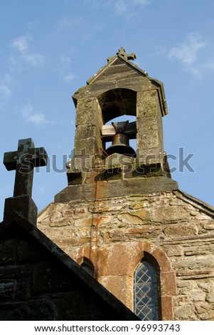 A shaded cross leads to a church bell tower with bell and chain backed by a blue sky.