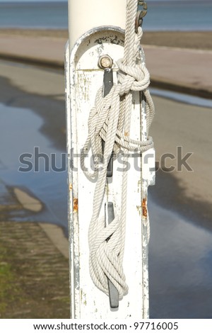 A white flag pole base with a white rope tied off on fixings.