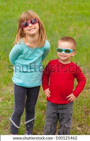 Brother and sister posing outside with sunglasses on their eyes on beautiful spring day.