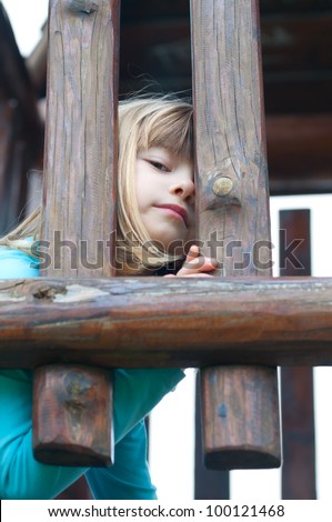 Cute little girl peeking out through wooden bars.