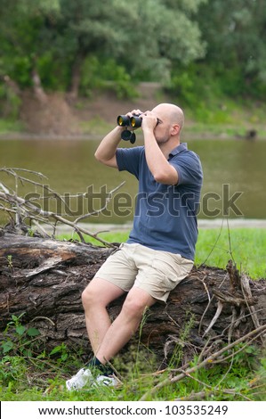 Slim bald man watching the nature through binoculars on cloudy spring day.