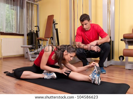 Beautiful young girl doing stretching exercises in the gym under supervision of her coach.