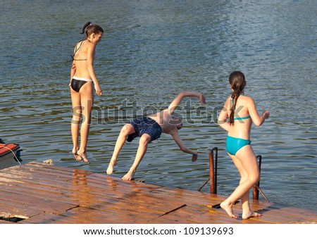 Teenage boy and teenage girls jumping into the river from old dock.