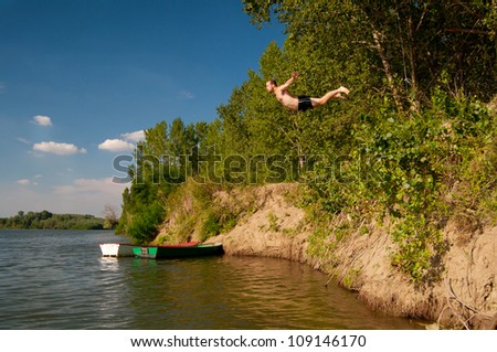Young man jumping from the shore into the river on sunny summer day.