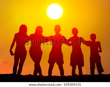 Silhouettes of boys and girls hugging on the beach on sunny summer day.