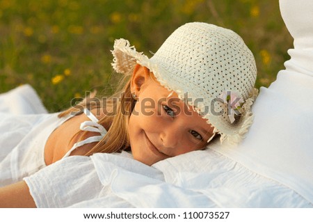 Cute little girl rests her head in her mothers lap on sunny summer day.