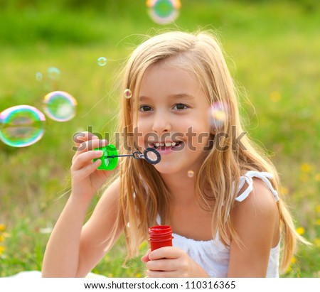 Cute little girl blowing soap bubbles on the meadow on sunny summer day.