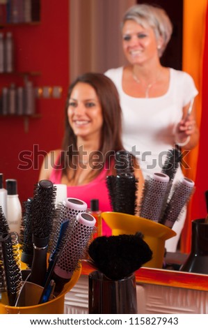 Hairdresser and beautiful girl having fun while making hair. Focus is on the combs and equipment in the bottom.