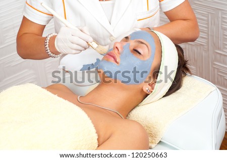 Beautiful young woman lying on massage table while facial mask is put on her face.