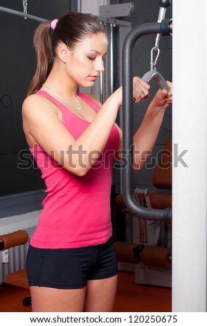 Beautiful young woman exercising arm muscles in the gym.