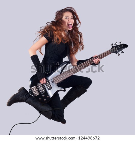 Beautiful girl with long red hair playing bass guitar and jumping in the air.