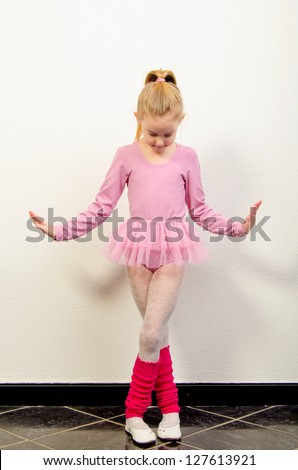 Cute little ballerina dancing against white wall.
