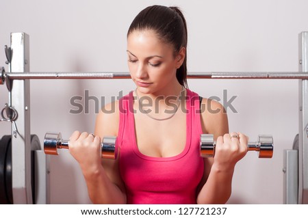 Beautiful young woman exercising with dumbbells in bodybuilding club.