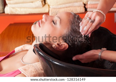 Beautiful young girl enjoying hair washing in hairdressing salon.