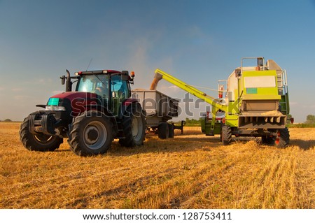 Modern combine harvester unloading grain into the trucks trailer on sunny summer day.
