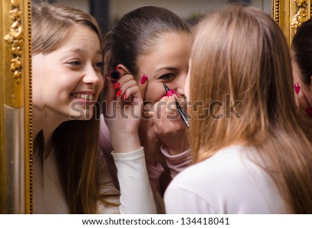 Beautiful teenage girlfriends having fun while putting make up in front of the old mirror.