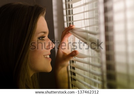 Beautiful girl looking through venetian blinds.
