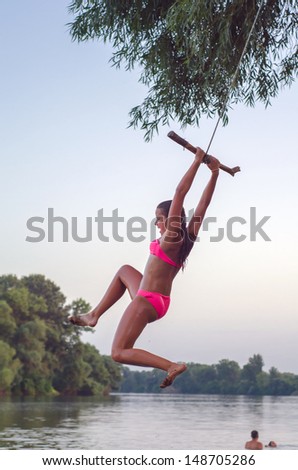 Teenage girl jumping into the river from the swinging rope on summer day.