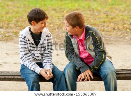 Two teenage friends talking while sitting on the bench in the park