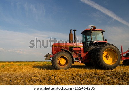 Modern red tractor on the agricultural field on sunny summer day.