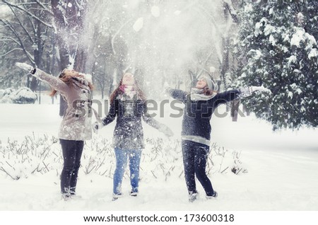 Three teenage girls throwing snow in the air on cold winter day.