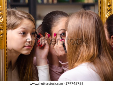 Beautiful teenage girlfriends having fun while putting make up in front of the old mirror.