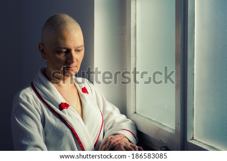 Bald woman suffering from cancer standing in front of the hospital window.