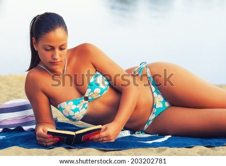 Beautiful girl reading book on the beach on sunny summer evening.