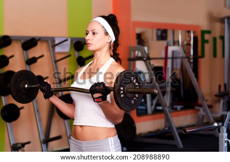 Beautiful young fitness girl lifting weights in the modern gym.