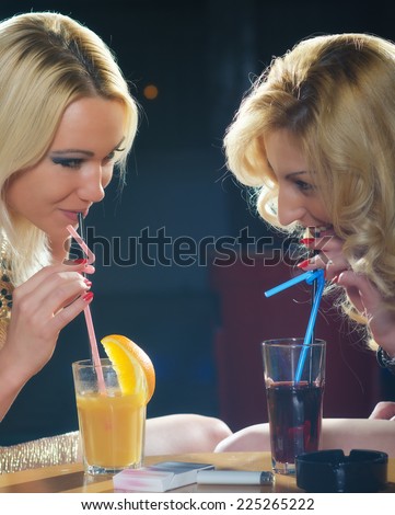 Two elegant ladies drinking cocktails at bar.