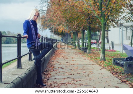 Beautiful young woman standing beside river on rainy autumn day.