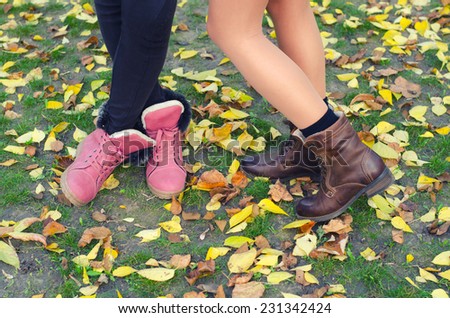 Legs and shoes of young girls standing on the dry leaves and grass on beautiful autumn day.